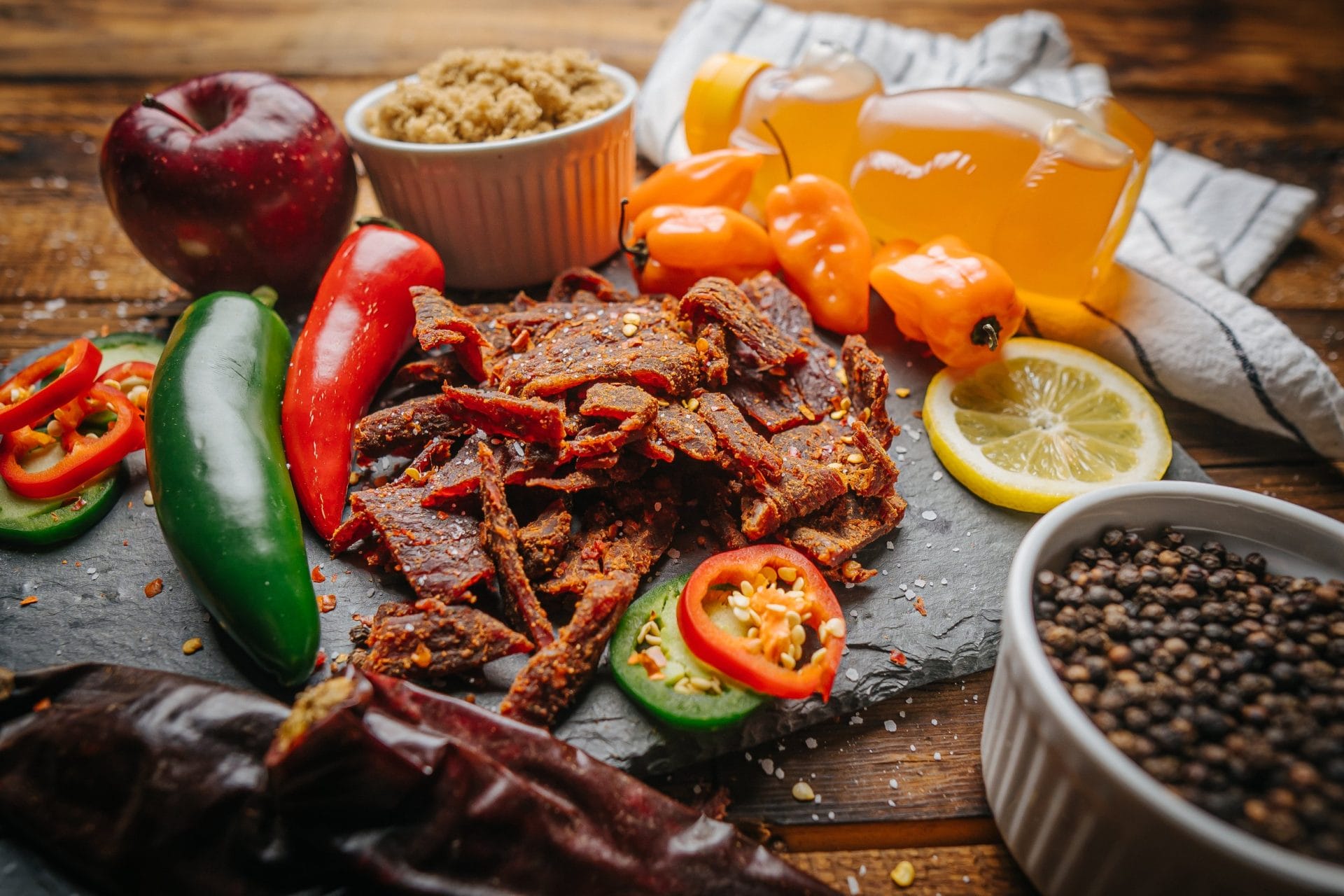 7-Alarm-1 7 Alarm beef jerky on slate with sliced peppers, habaneros, honey bear, lemon, and spices.