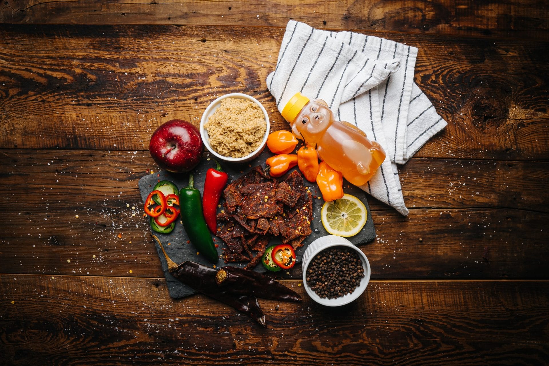 7-Alarm-2 7 Alarm beef jerky on slate with peppers, brown sugar, apple, honey bear, lemon, and spices.