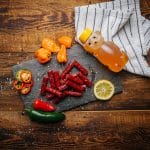 Glenwood honey habanero meat sticks on slate with sliced peppers, honey bear bottle, and lemon slice.