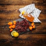 Honey Habanero beef jerky with habanero peppers, honey bear bottle, and lemon on rustic slate board.