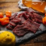Honey Habanero beef jerky pieces on slate with habanero peppers, lemon slices, and honey in background.