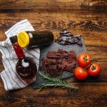 Smoke Pit beef jerky on slate with tomatoes, rosemary, dried chiles, and barbecue sauce on rustic wood.