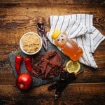 Sweet & Spicy beef jerky with honey, brown sugar, chiles, apple, and lemon on rustic board.