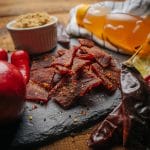 Sweet & Spicy beef jerky pieces on slate with red chiles, apple, lemon, brown sugar, and honey.